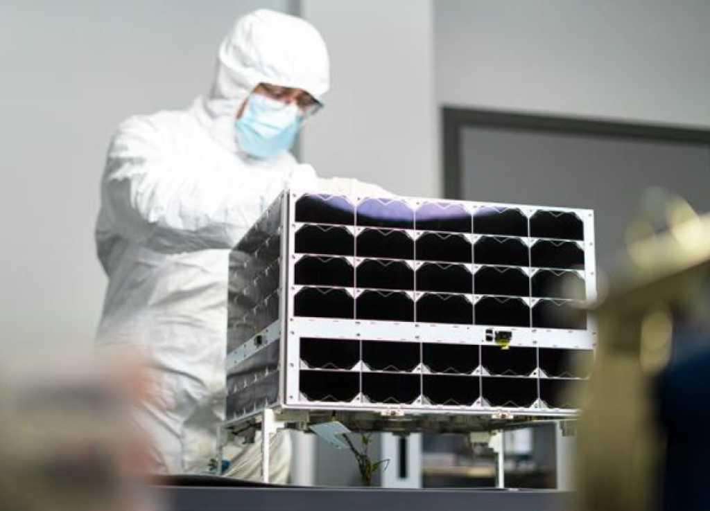 en mann i hvit drakt står bak en satellitt