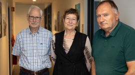 Tre eldre mennesker, to menn og en kvinne, oppstilt i en korridor