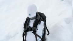 Overkroppen på en dukke står utplassert i snøen. På seg har den en ryggsekk med produktet Safeback