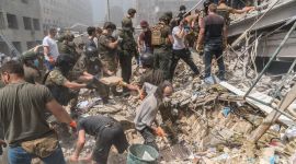 Mennesker graver i bygningsrester etter et missilnedslag. Det er støv i luften. Sommer.