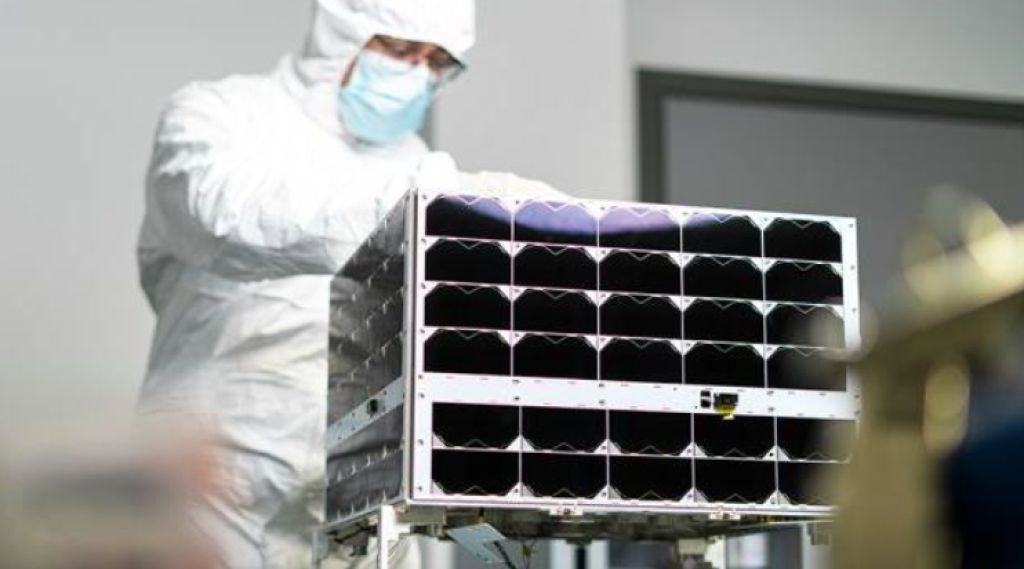 en mann i hvit drakt står bak en satellitt