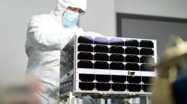 en mann i hvit drakt står bak en satellitt