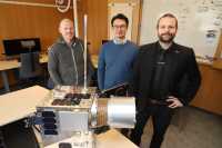 Tre it-utviklere foran en kopi av satellitten NorSat-4.