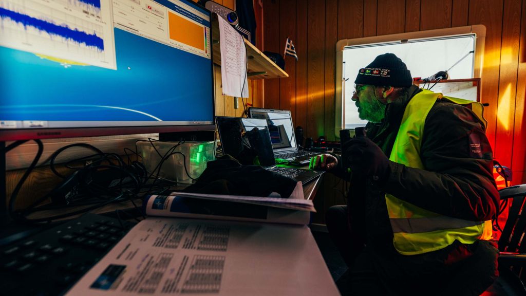 Mann i refleksvest sitter foran flere PC-er innendørs.