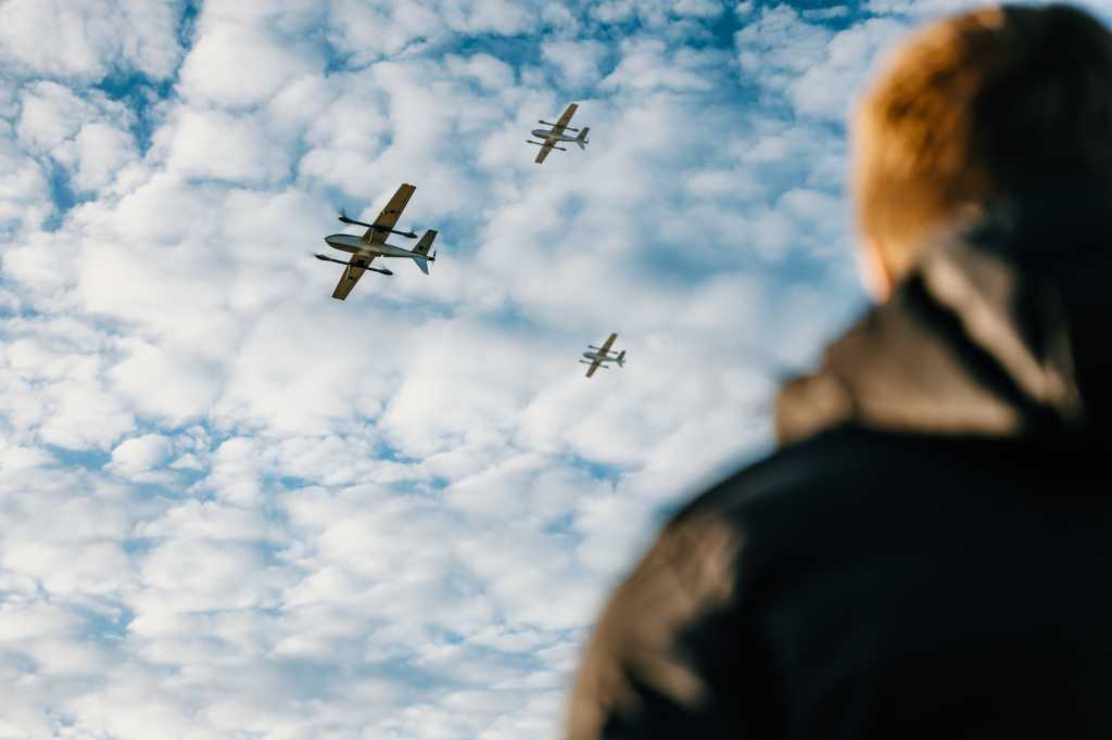En person ser opp på tre droner som flyr forbi.