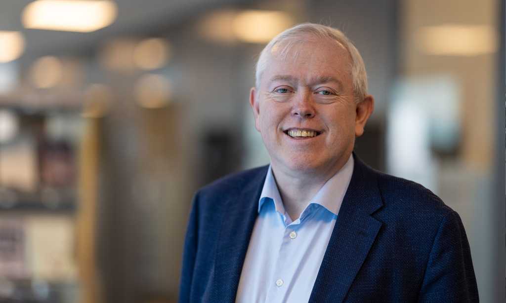 Portrett av en smilende Bjørn Olav Knutsen. Han har på blå skjorte og en blå dressjakke.