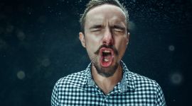 Mann nyser, hoster eller roper mens det spruter dråper ut av munnen hans.