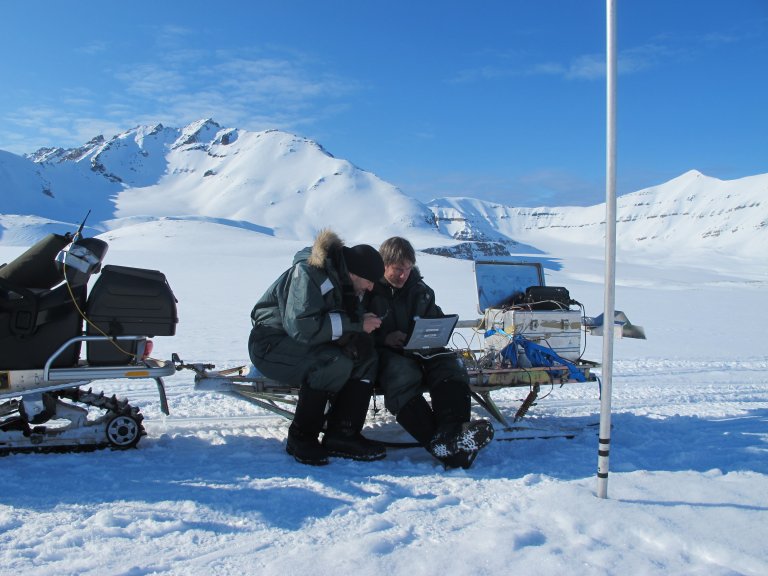 To forskere sitter med en laptop på en snøscooterslede