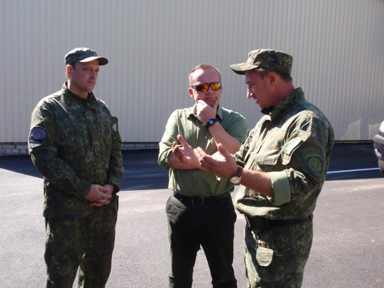 Tor Bukkvoll står sammen med to menn i uniform som forklarer ham noe