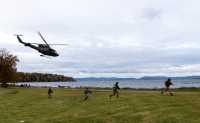 Fire bevæpnede spesialsoldater løper over en gresslette. Helikopteret som nettopp har satt dem av, flyr videre ut over fjorden i bakgrunne.