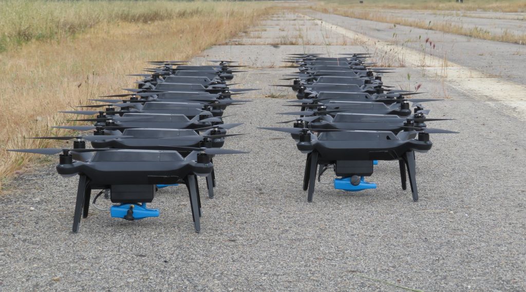 Mange droner oppstilt på bakken. Foto