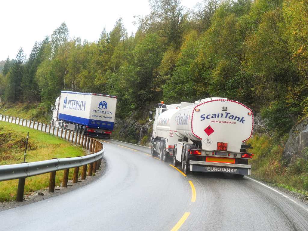 To digre lastebiler på en smal og svingete europavei.  Veien er så smal at det ene vogntoget krysser midtlinjen. Høst. regn. 