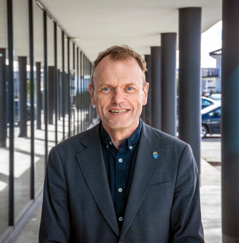 Portrett av Jan Erik Torp. Utendørs. Sommer. Han står i en søylegang.