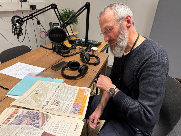 Forsker sitter i podkaststudio og leser i avis.