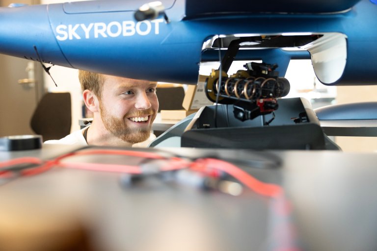 Student ser på en sensor som henger under en drone. 