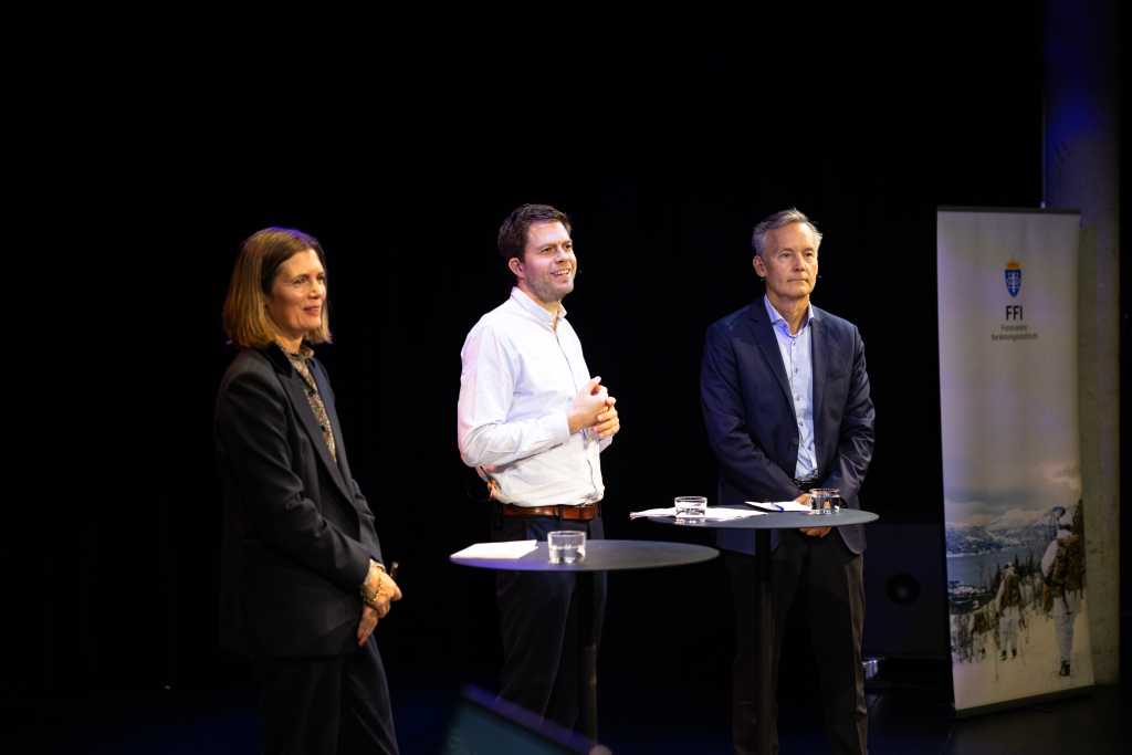 Tre personer på scenen i Deichmanssalen. Svart bakgrunn.