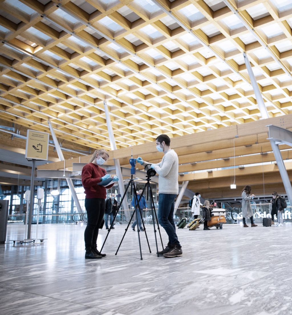 Two researchers standing up close to testing equipment in a large airport hall.
