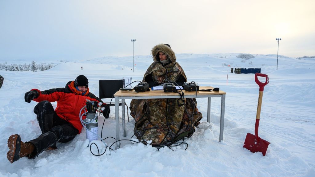two men by a desk in the middle of no where in deep snow doing tests