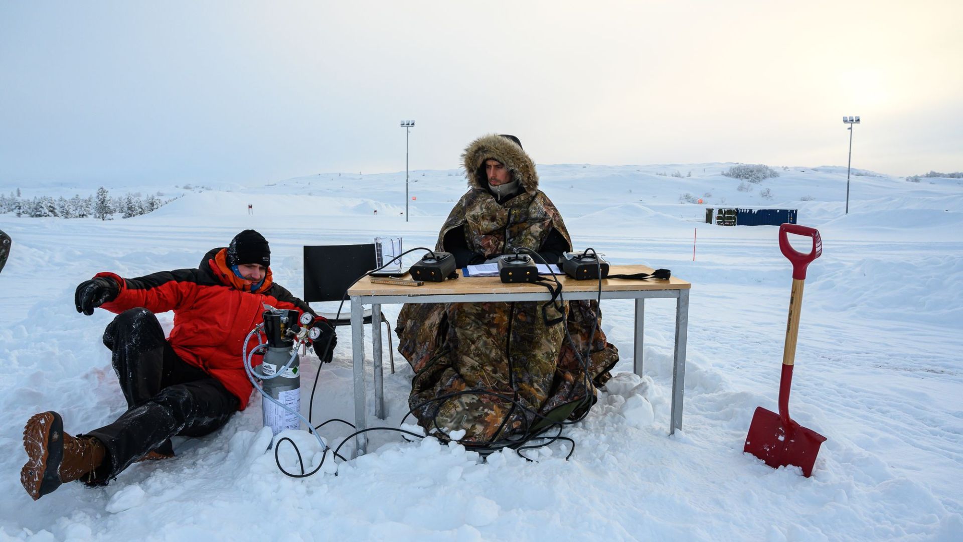 two men by a desk in the middle of no where in deep snow doing tests