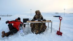 two men by a desk in the middle of no where in deep snow doing tests