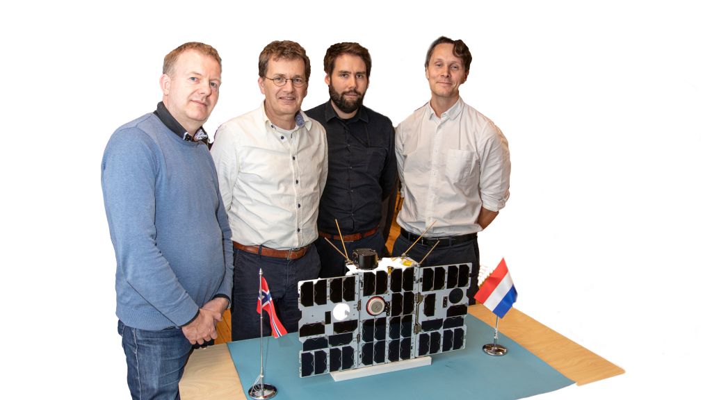 Four men behind a table with Norwegian and Dutch flags and a model of the satellite