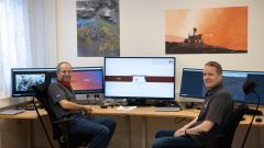 to forskere sitter foran datamaskiner og plakater av Rimfax og Mars