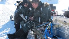 To men sitting on a snowmobile-sledge working on a laptop