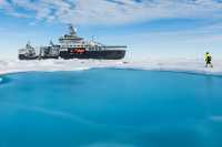 The research vessel Kronprins Haakon in the Arctic Ocean, with a person walking on the ice to the right of the ship.
