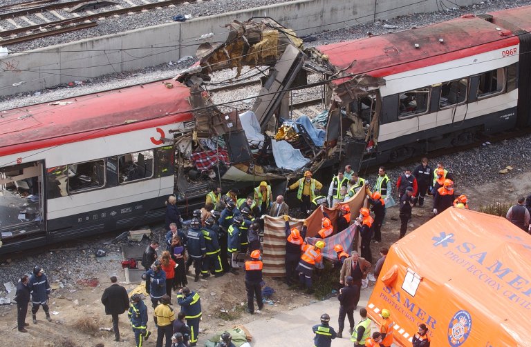 A train having a whole in it from a bomb. People standing on the outside.