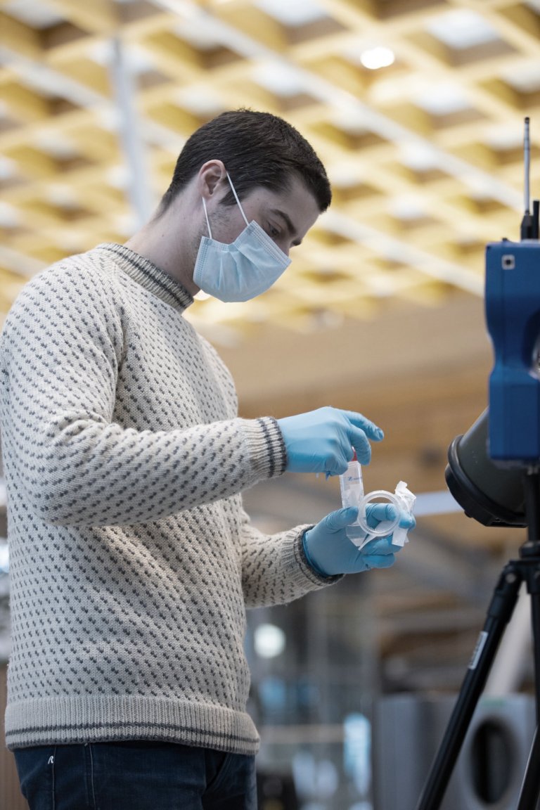 Researcher wearing face mask and gloves holding a testing tube.