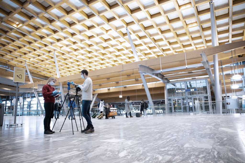 Two researchers standing up close to testing equipment in a large airport hall.