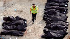 Man walking past rows of black body bags