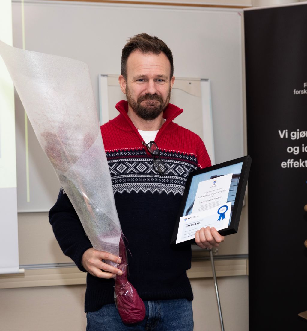 En mann står med en blomsterbukett og diplom og smiler til fotografen
