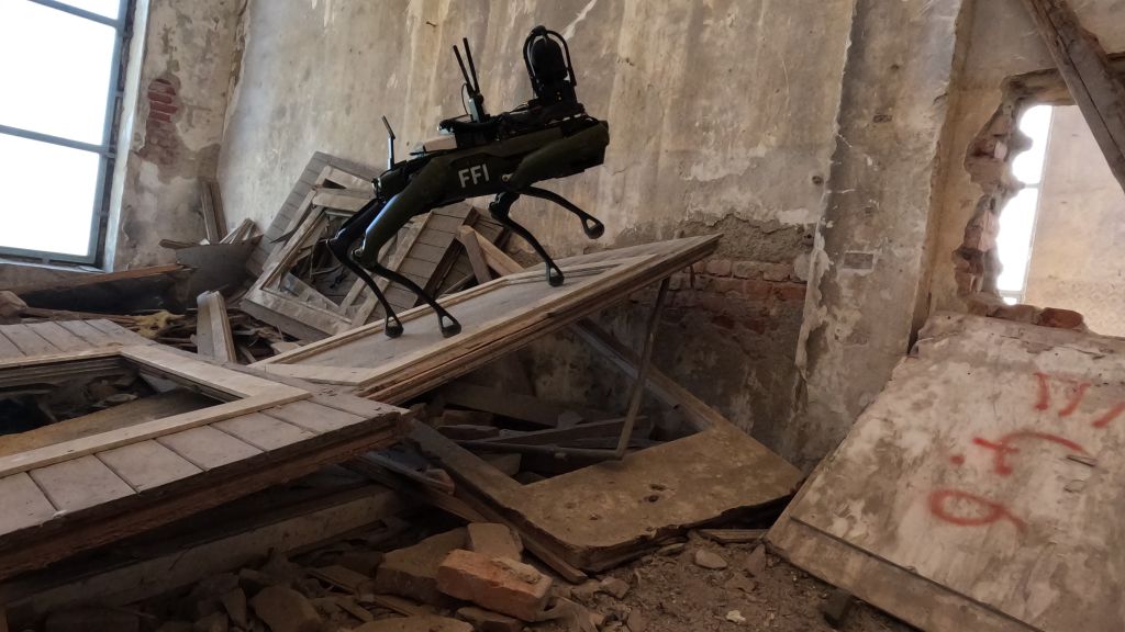 Robothund går på plankehaug i husruin. Foto