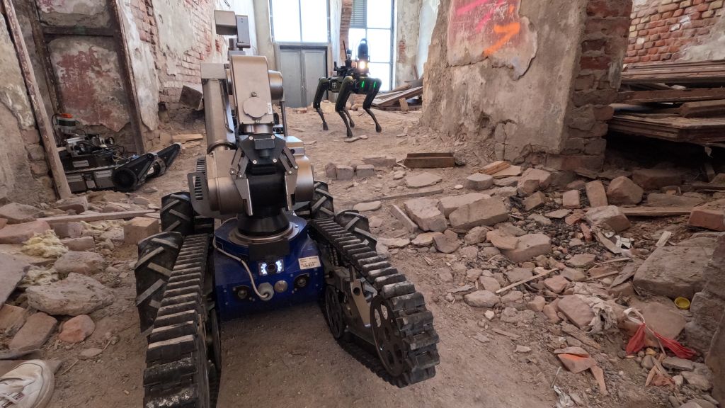 Liten selvkjørende beltevogn og robothund i husruin. Foto