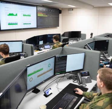 Bilde fra cyybersikkerhetssenteret på Jørstadmoen. Menn i uniform følger med på skjermer.