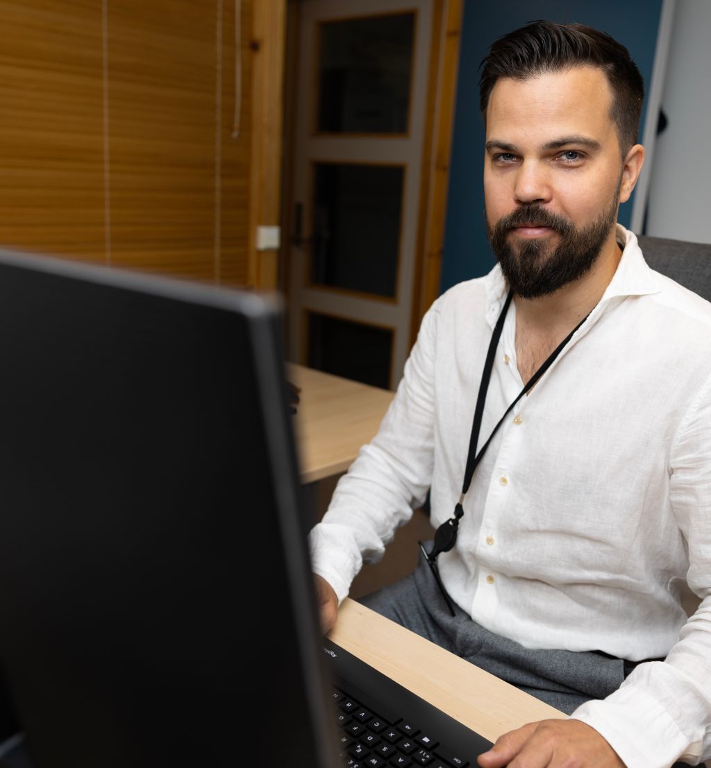 Mann i hvit skjorte sitter bak tastatur og ser rett i kamera