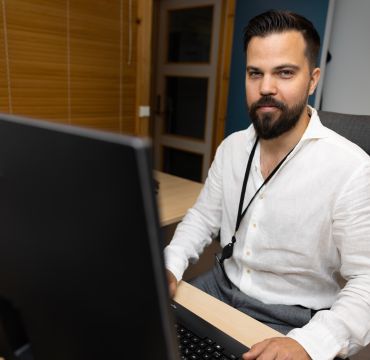 Mann i hvit skjorte sitter bak tastatur og ser rett i kamera