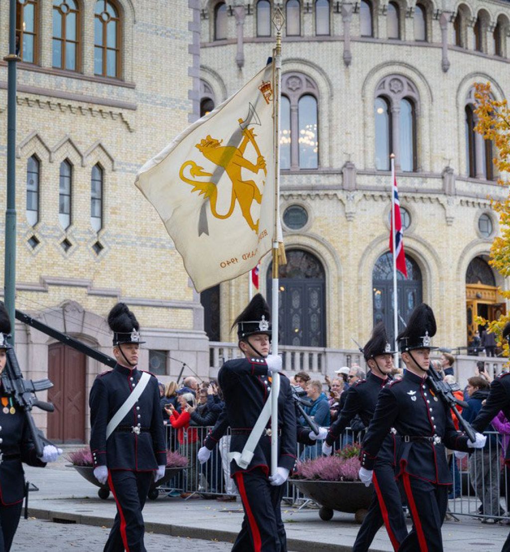 Garden marsjerer forbi Stortinget med en fane.