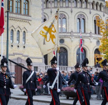 Garden marsjerer forbi Stortinget med en fane.
