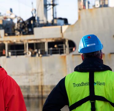 et militært fartøy i en havn med sivile med ryggen til kamera