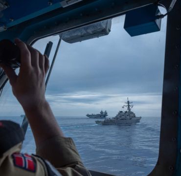 En soldat bruker kikkerten og ser to marinefartøy foran seg.