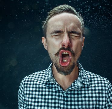 Mann nyser, hoster eller roper mens det spruter dråper ut av munnen hans.