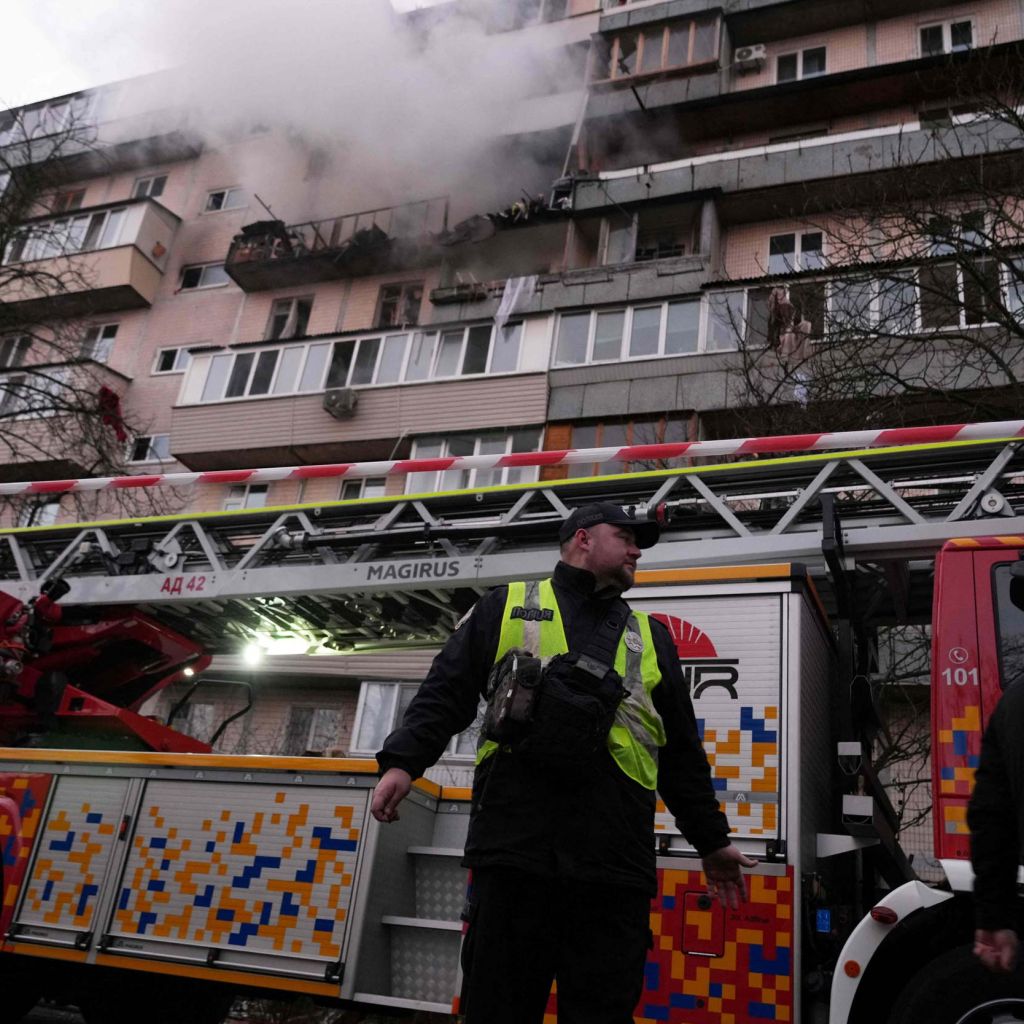 En politimann står foran en brannbil. I bakgrunnen røyk fra en boligblokk.
