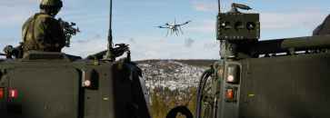 En soldat på et kjøretøy sikter på en drone med et våpen.