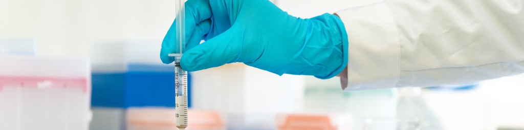 en hånd med hanske i et laboratorium tar noe i et reagensrør 