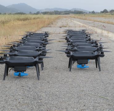 Mange droner oppstilt på bakken. Foto
