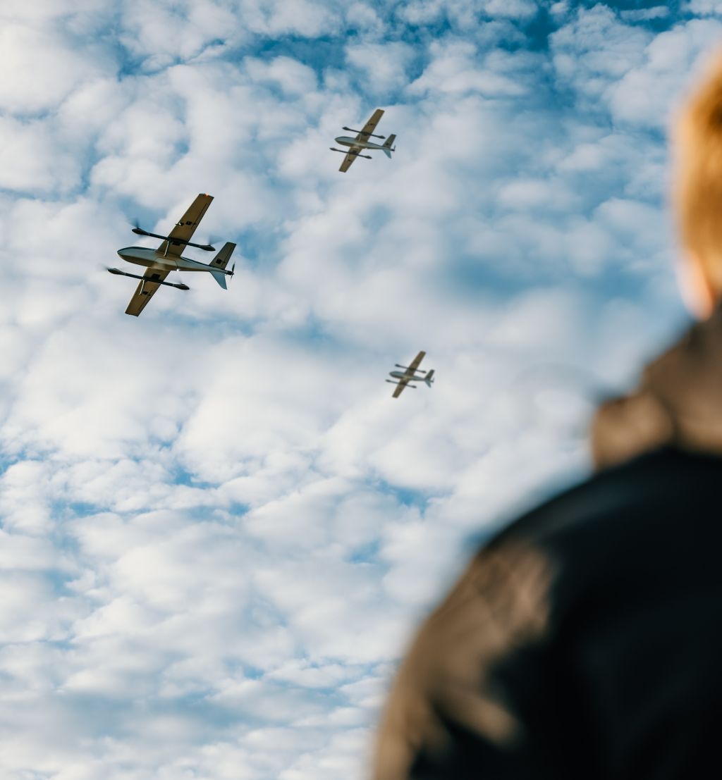 En person ser opp på tre droner som flyr forbi.