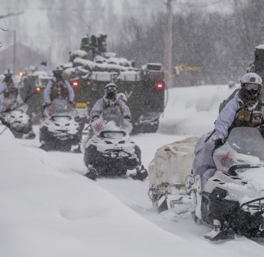 Soldater på snøscooter og cv-90 panservogner i kolonne i tett snøvær.