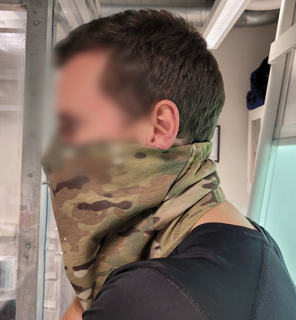 En testperson står med en SAFEgaiter kamuflasbuff med åndedrettsvern i ett av FFIs laboratorier. Ansiktet er sladdet.